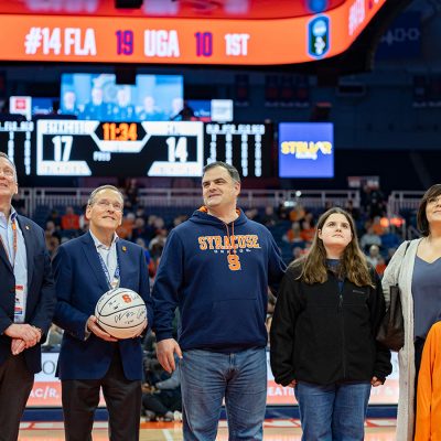 Zellar family stands on court of JMA Wireless Dome as Andrew Zellar named Hometown Hero. Two men in suits, one holding a basketball, stand to the right of Zellar.