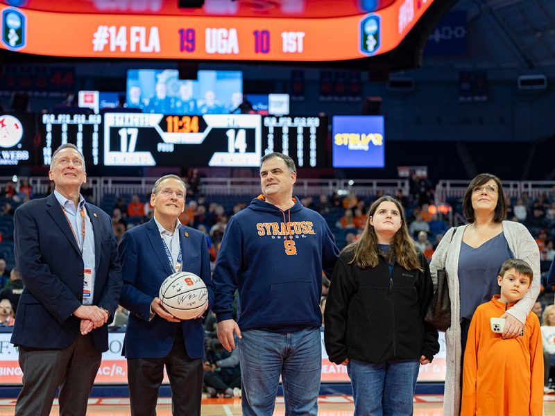 Zellar family stands on court of JMA Wireless Dome as Andrew Zellar named Hometown Hero. Two men in suits, one holding a basketball, stand to the right of Zellar.