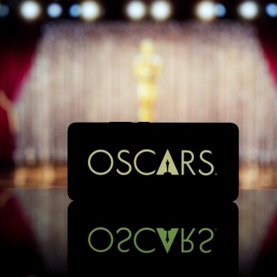 A smartphone displaying the Oscars logo in front of a stage with red curtains and a gold statue in the background.