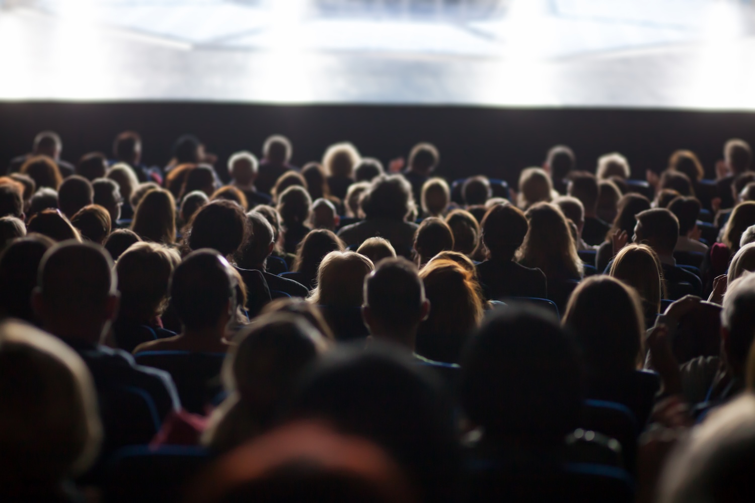 A full theater audience seated and facing a brightly lit stage.