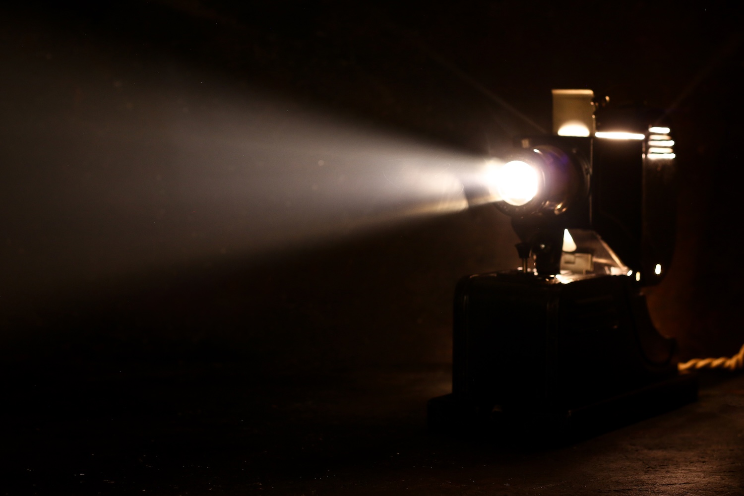 A vintage film projector casting a bright beam of light in a dark room.
