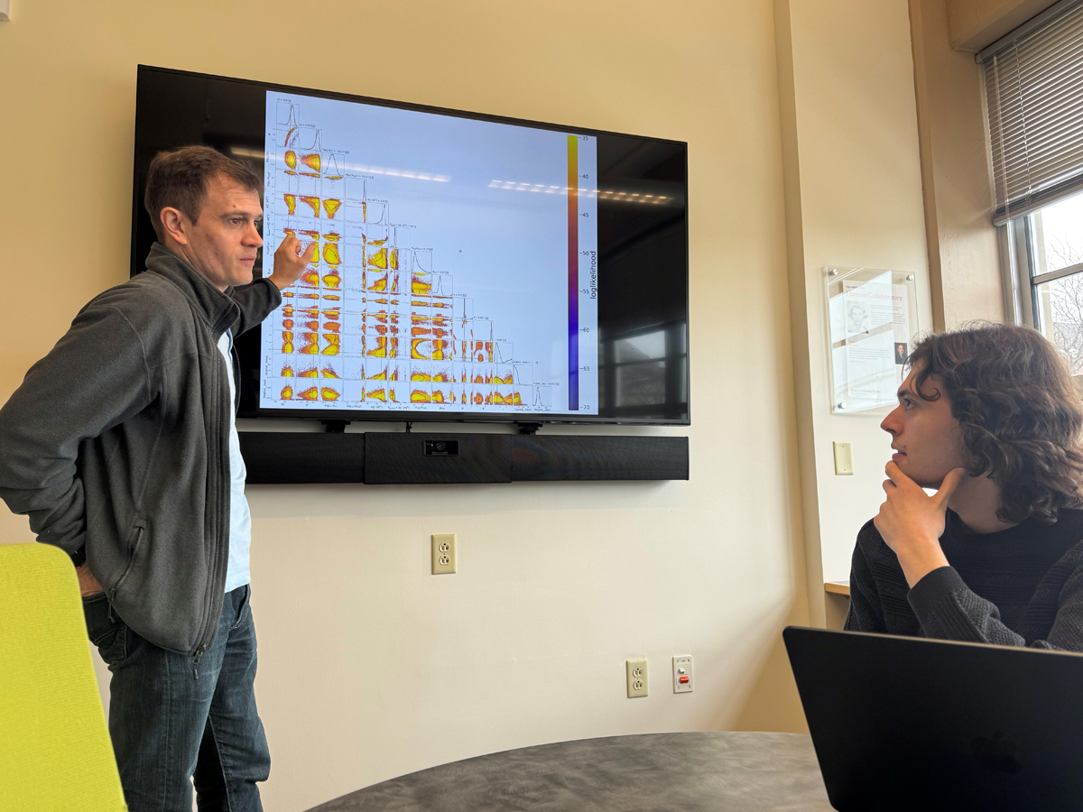 A researcher points to a heatmap matrix on a display screen while a student listens attentively.