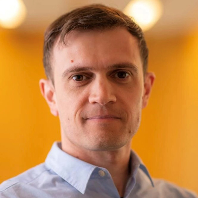 A person poses for a headshot in front of a yellow wall.