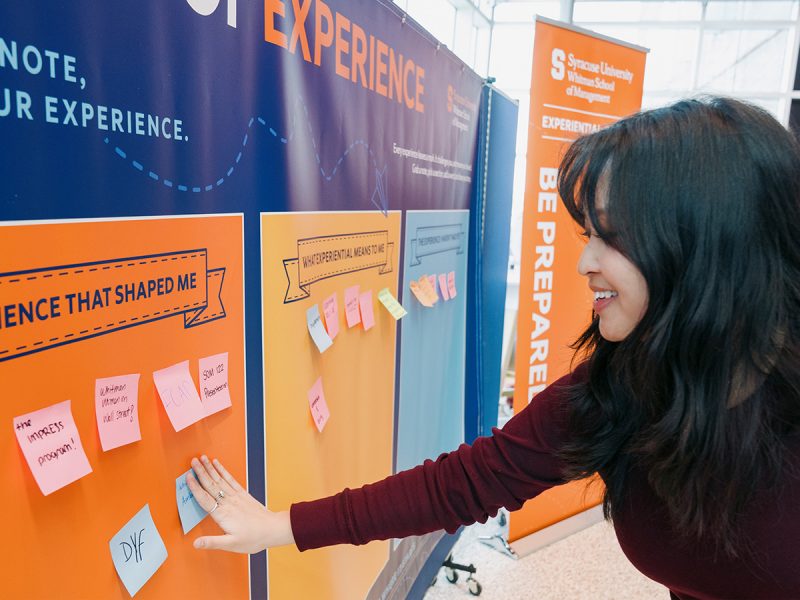 Campus experiential learning display with colorful panels and sticky notes as a participant adds feedback