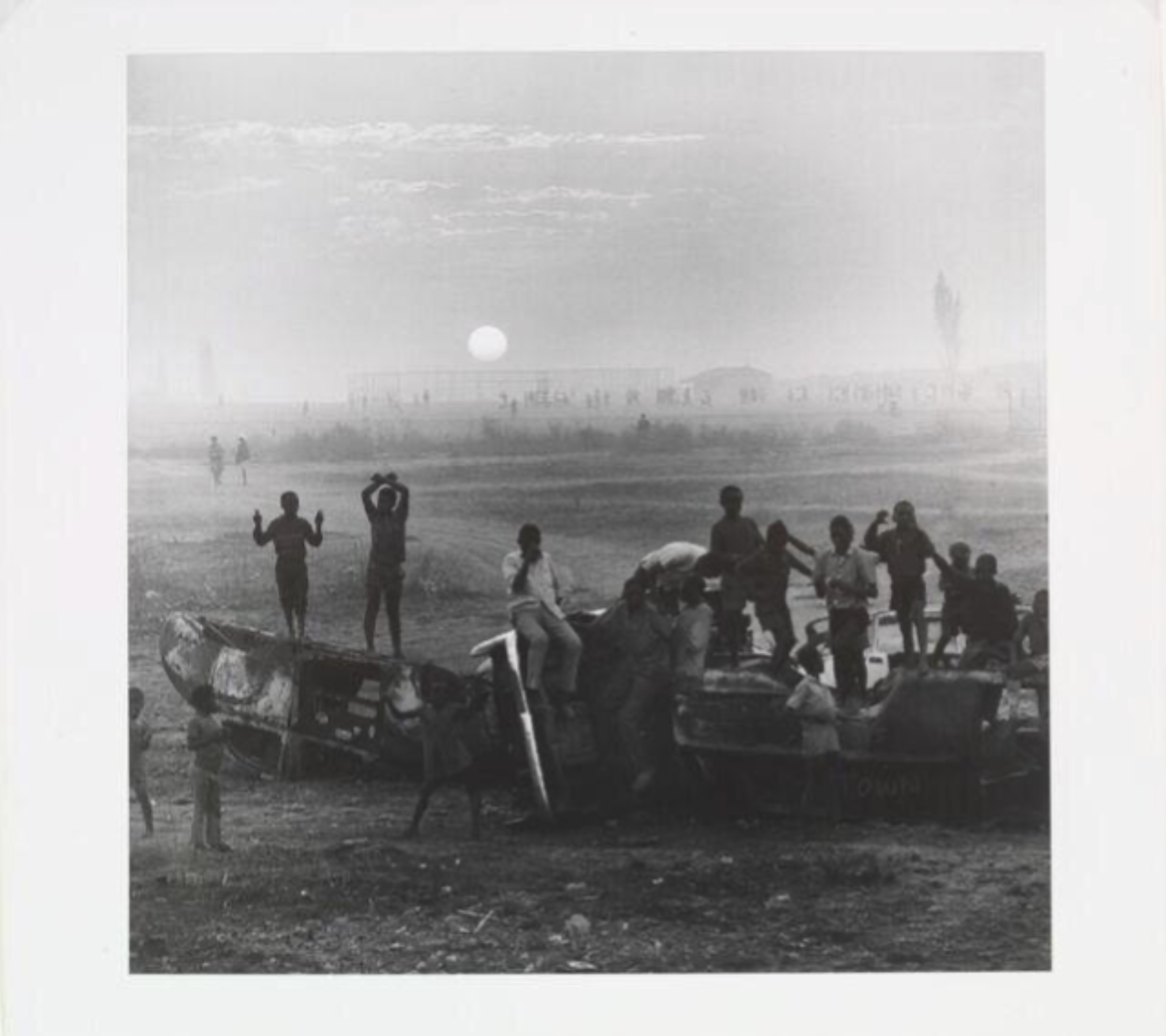 Children climb and play on wrecked cars in an open field as the sun sets over the hazy horizon in Soweto, in David Goldblatt's "Sunset over the Playing Fields of Tladi, Soweto, Johannesburg