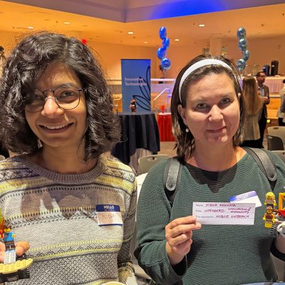 Two women in a brightly room, holding small Lego models they made. Both are smiling.