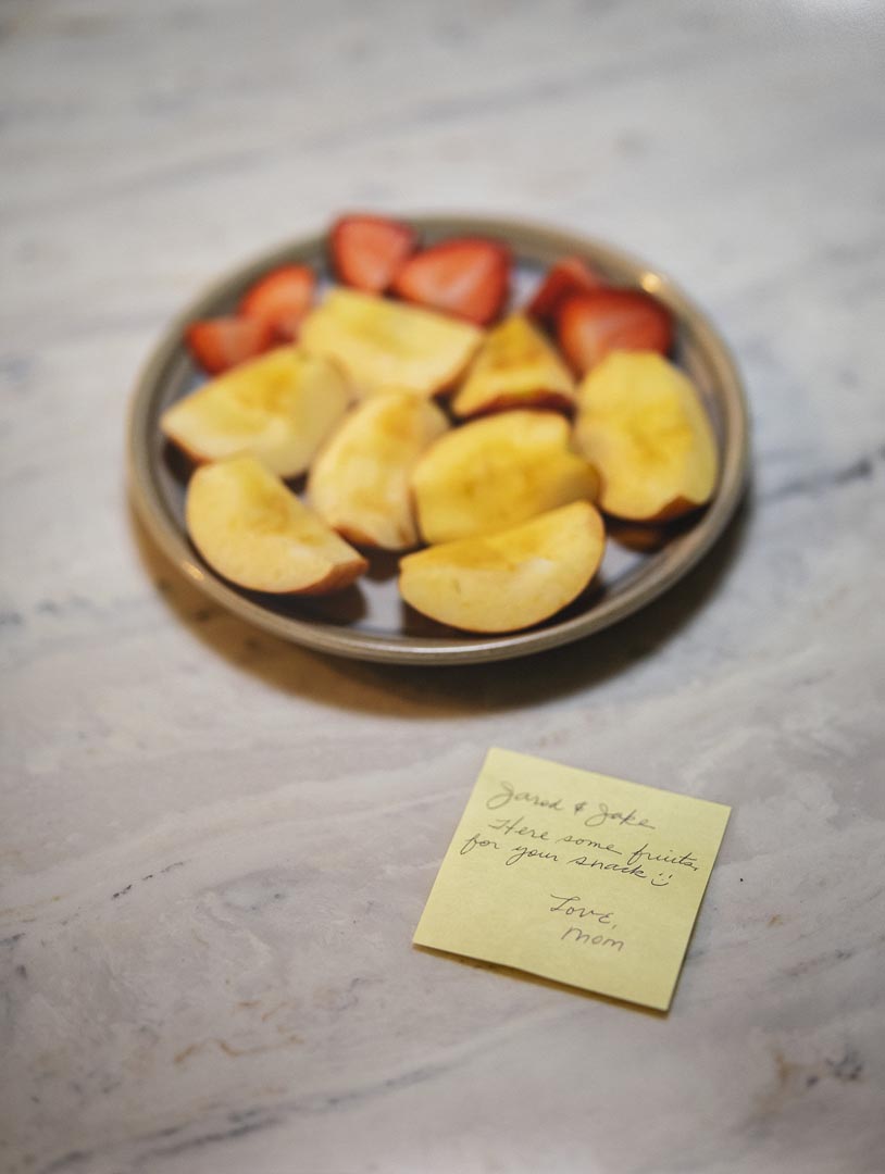 A plate of sliced fruit sits on a marble surface, with a yellow sticky note in the foreground 