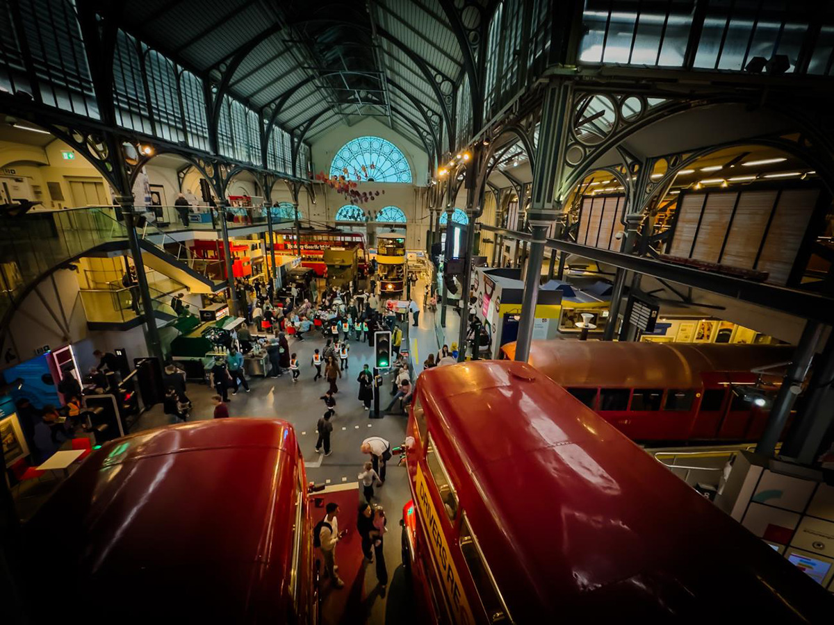 Interior view of the London Transport Museum, featuring iconic red double-decker buses on display beneath a Victorian iron-and-glass roof, with visitors exploring the multi-level exhibition hall in Covent Garden.