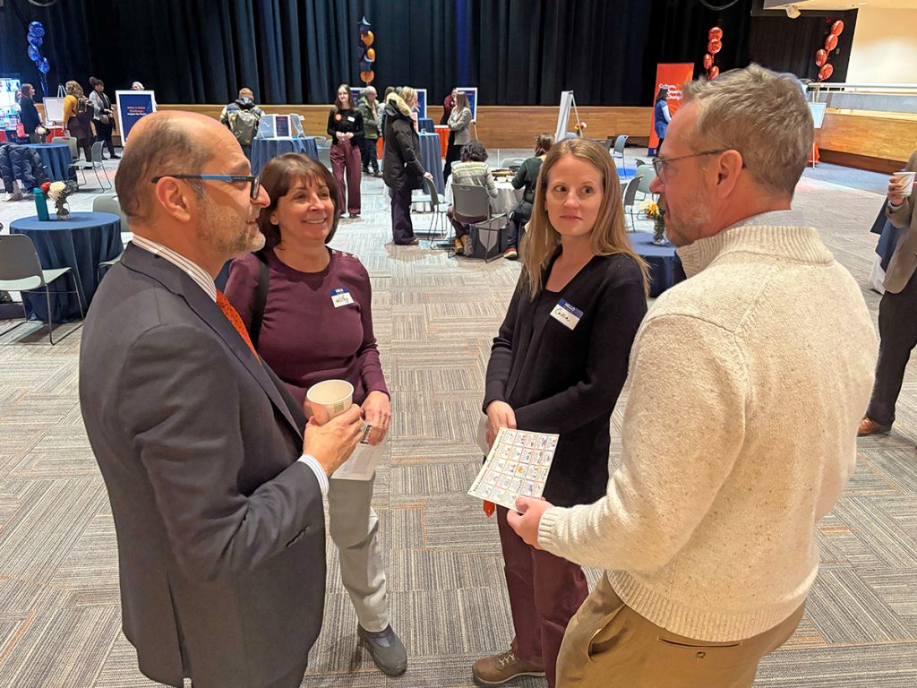 Four people in a brightly room, standing in a circle and talking.