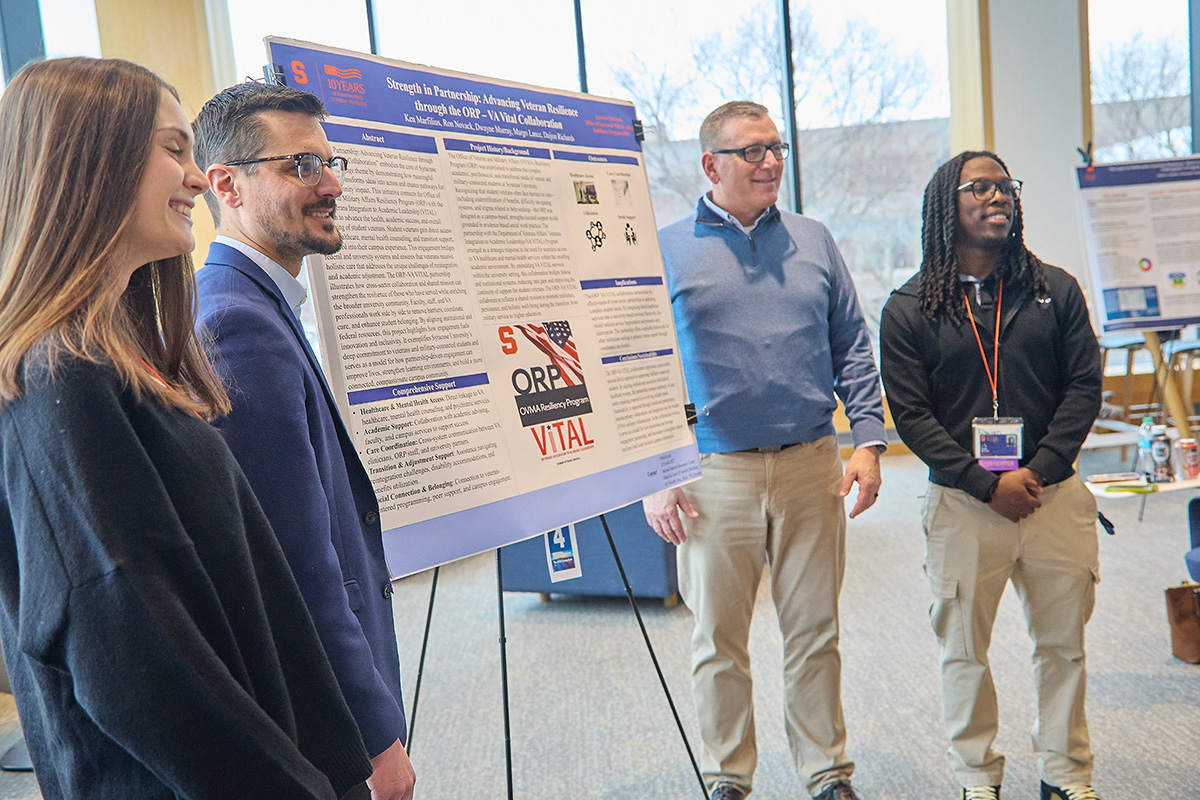 Group standing beside an academic research poster displayed on an easel during a campus event