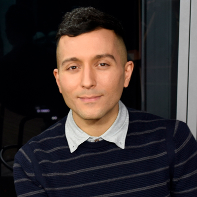 A person poses for a headshot wearing a navy striped sweater against a dark background.