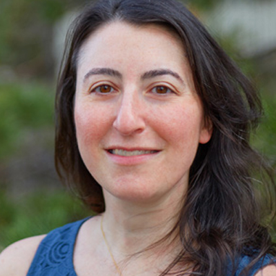 A person smiles for a headshot while standing outside.
