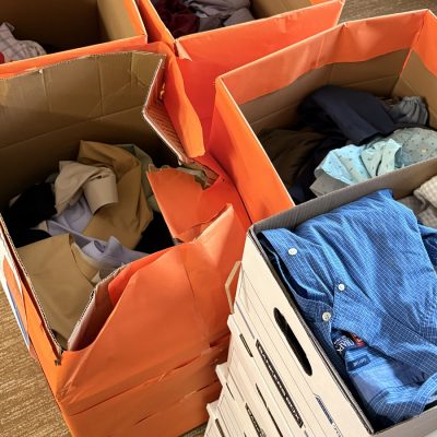 Several boxes filled with donated button-down shirts and clothing collected for a clothing drive.