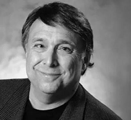 A black-and-white portrait of a man with sideswept medium length dark hair smiling warmly.