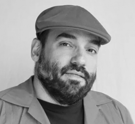 A black-and-white portrait of a bearded man wearing a flat cap.