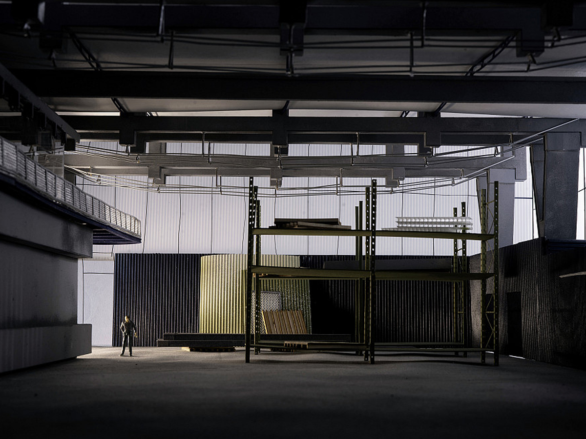 Architectural scale model of a dark industrial warehouse interior with a small human figure for scale.