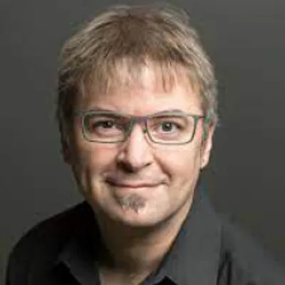 A person wearing a dark shirt shown against a plain background.