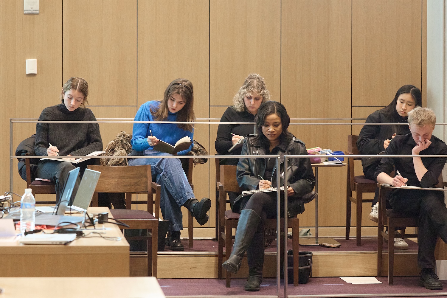People seated in a courtroom gallery, sketching in notebooks during a hearing.