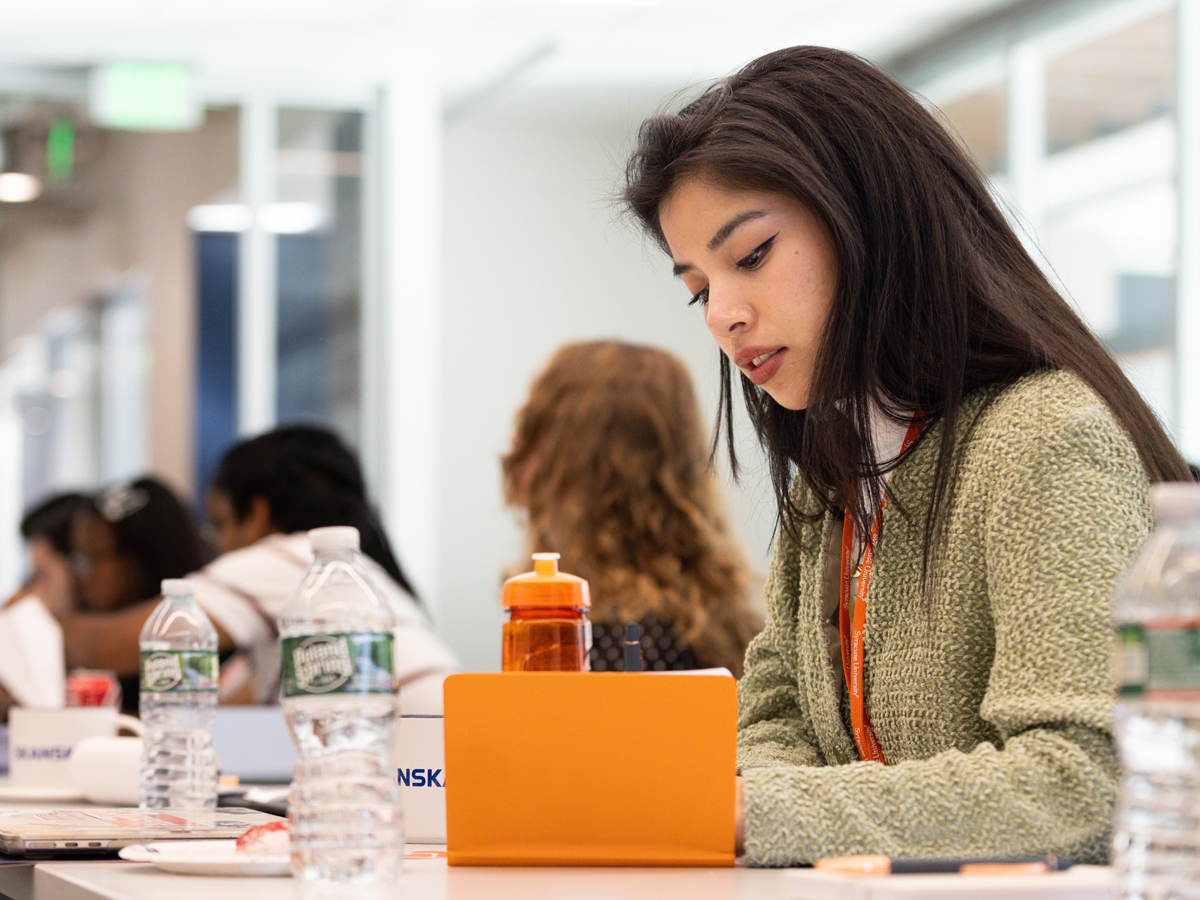A student wearing an orange lanyard works on a laptop at a table during a career-related event.