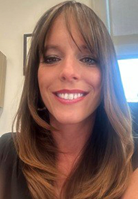 A person smiles for a headshot inside their office.