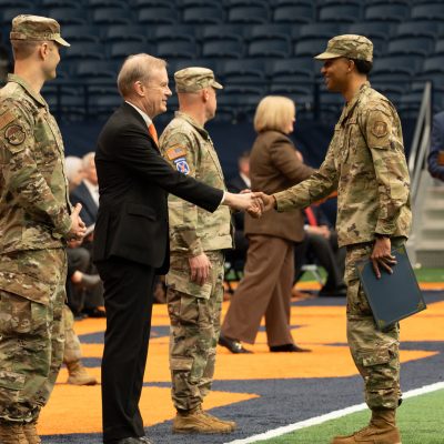 Chancellor shakes hands with ROTC cadets in camouflage uniforms on the field inside the JMA Wireless Dome.