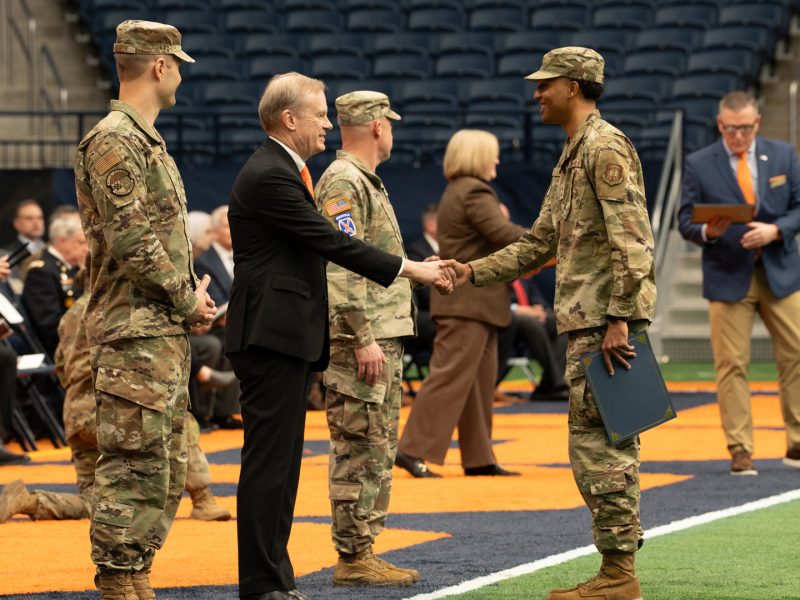 Chancellor shakes hands with ROTC cadets in camouflage uniforms on the field inside the JMA Wireless Dome.
