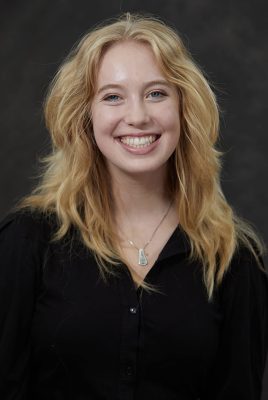 Professional headshot of a smiling woman with shoulder-length blonde hair against a dark background
