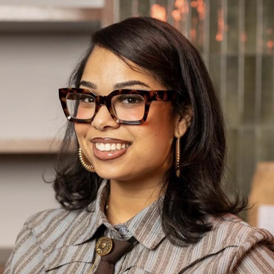 A student smiles wearing tortoiseshell glasses and gold earrings in a casual headshot.
