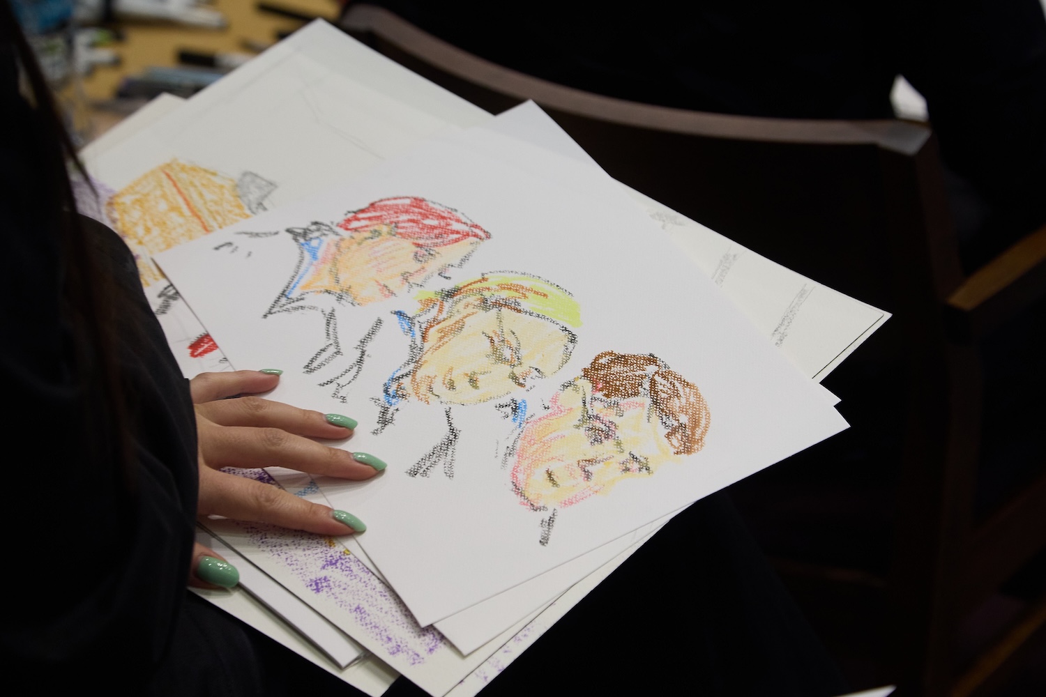 Hand holding a stack of colorful courtroom portrait sketches drawn in pastel.