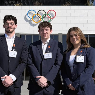 Three students wearing sport jackets pose outside of the Olympic Museum.