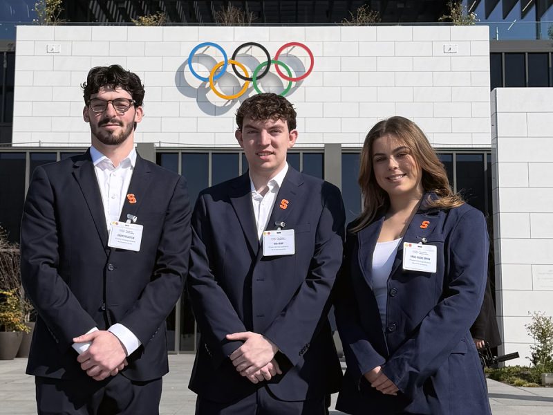 Three students wearing sport jackets pose outside of the Olympic Museum.