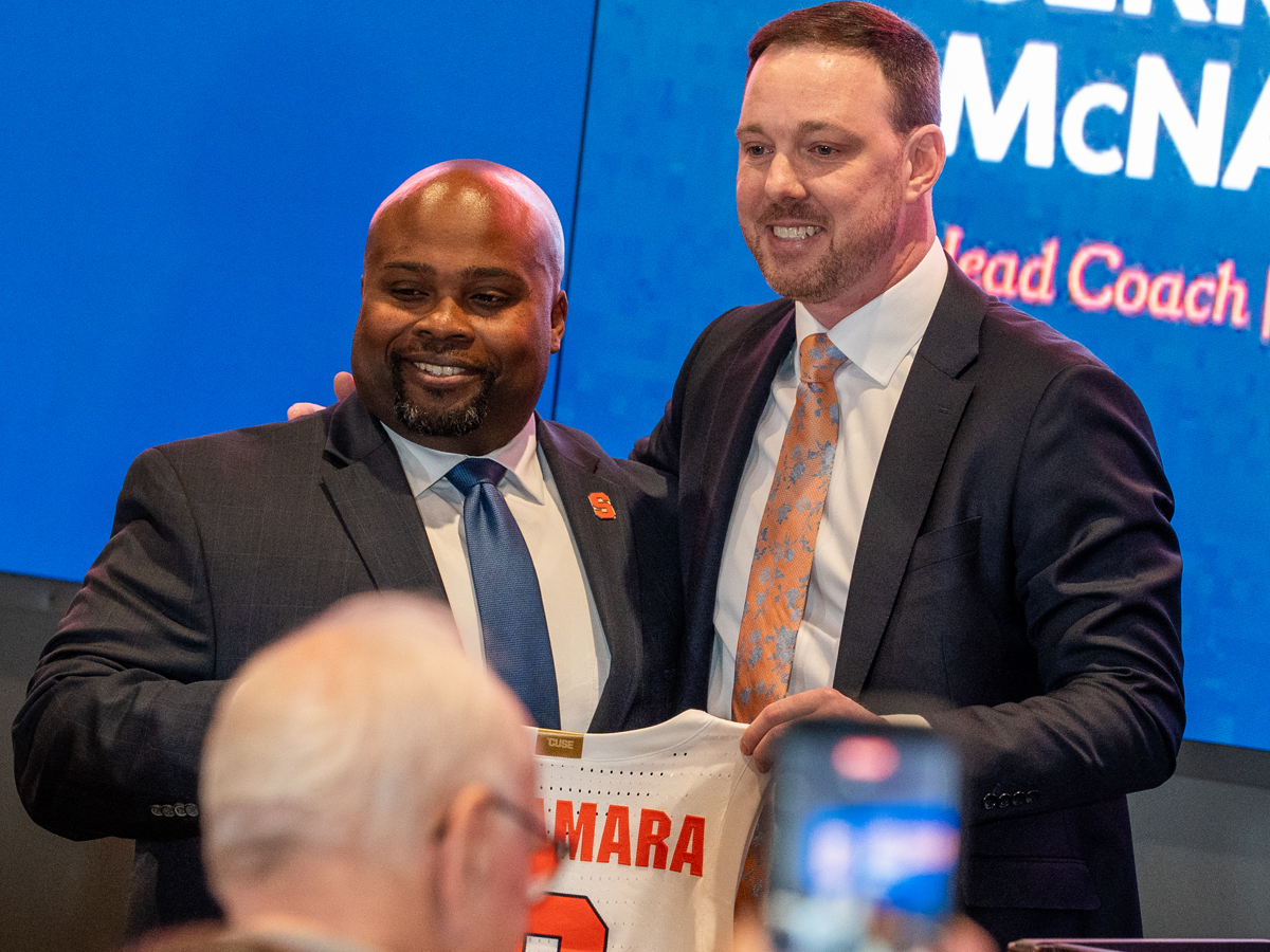 Two men smile while holding a Syracuse basketball jersey reading "McNamara" at an introductory press conference.