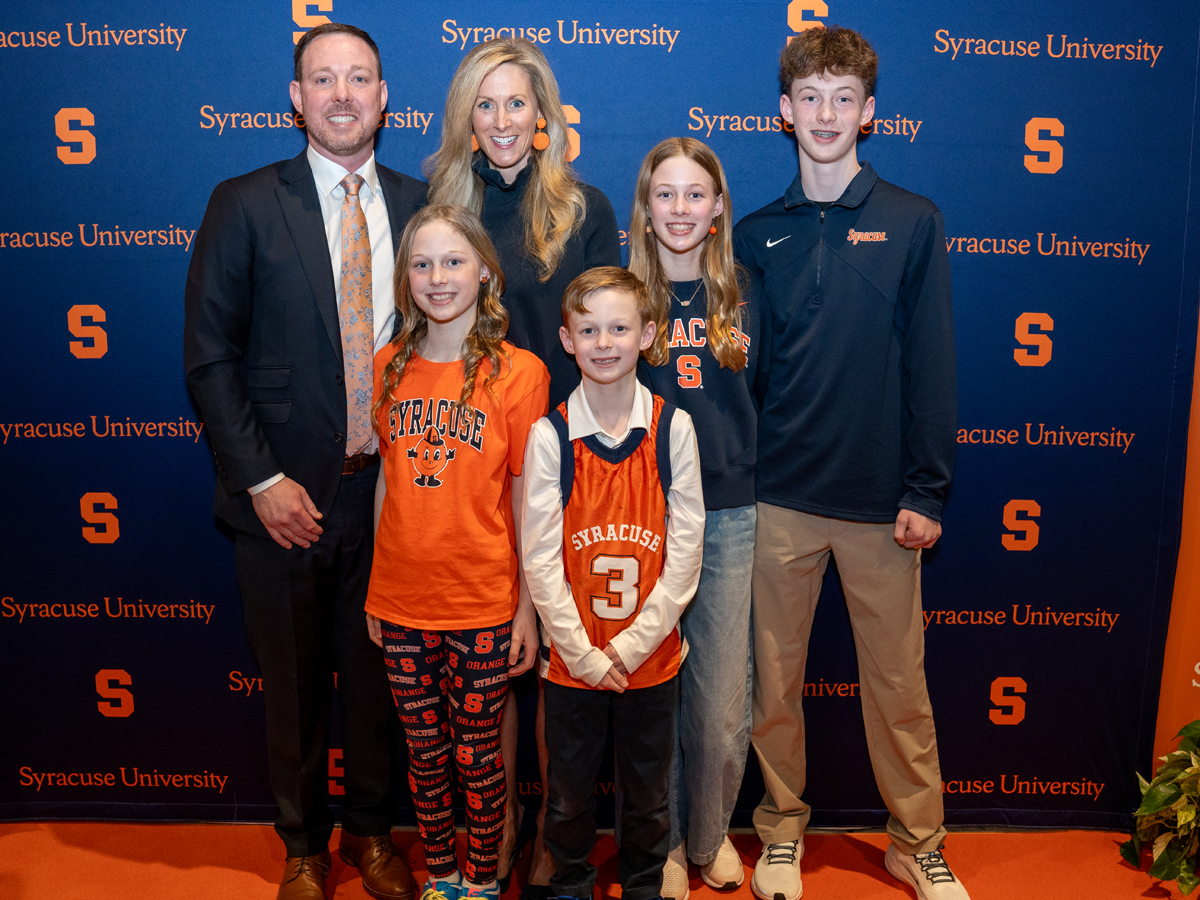 A man, woman and four children pose together in front of a Syracuse University step-and-repeat backdrop.