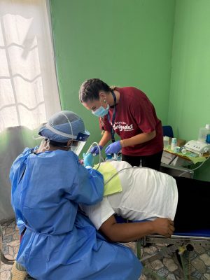 A masked Medical Brigades volunteer assists a dentist performing a procedure on a patient in Panama.