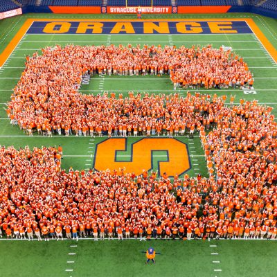 Large crowd wearing orange forms a block ‘S’ on the Syracuse University football field