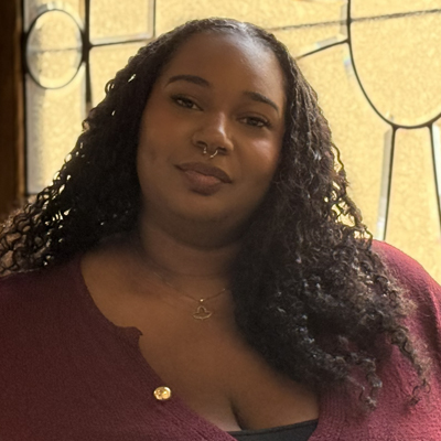 A student poses in a maroon top before a stained glass window in a headshot.