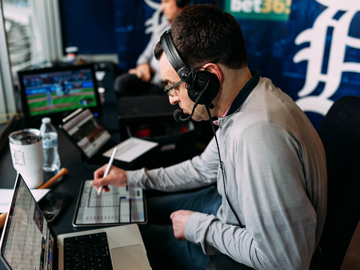 Jason Benetti wears a headset and takes notes on a tablet during a Detroit Tigers broadcast.