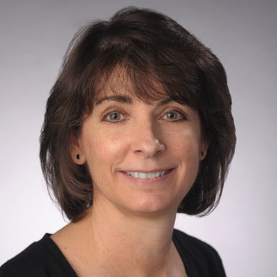 A person smiles while posing for a headshot in front of a white backdrop.
