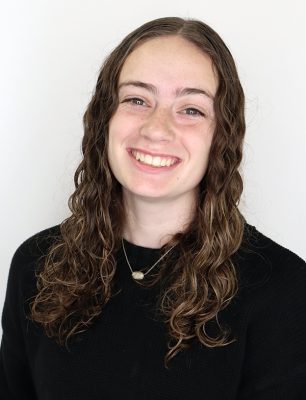 Smiling person with long wavy hair wearing a black top against a white background