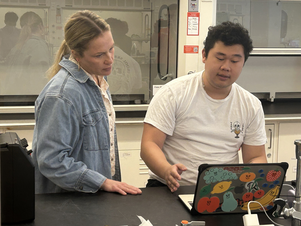 A professor and student review research data on a laptop together in a forensic science laboratory.