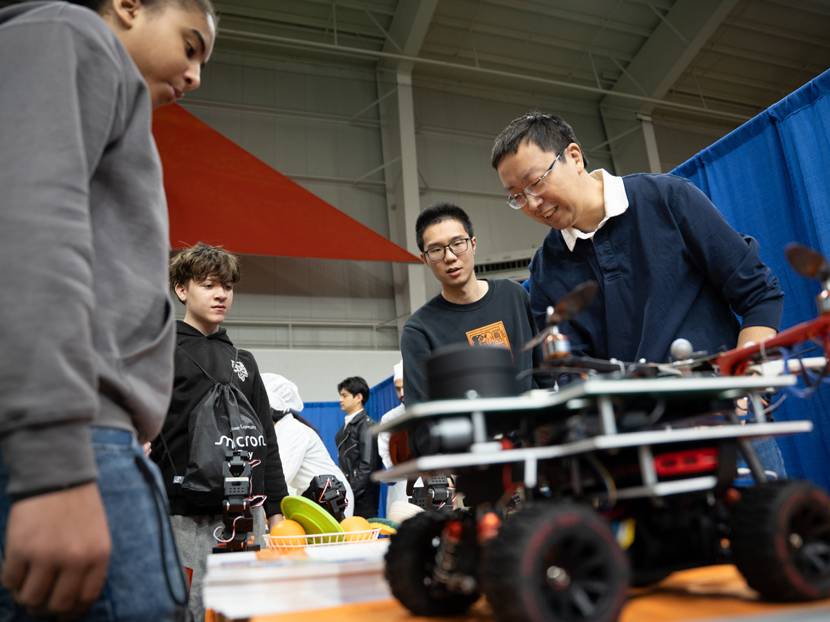 Three students and an instructor lean over a wheeled robot during a demonstration at Micron Day.
