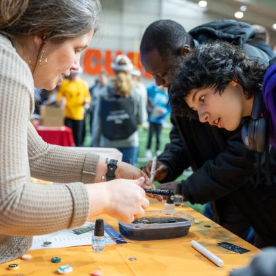 Students and an exhibitor lean over a table during a hands-on science demonstration at Micron Day.