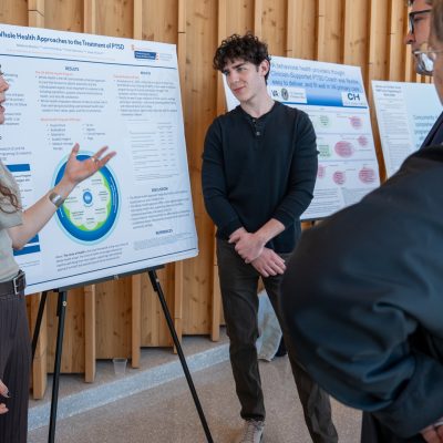 Student presents PTSD research poster to two attendees at an academic symposium.