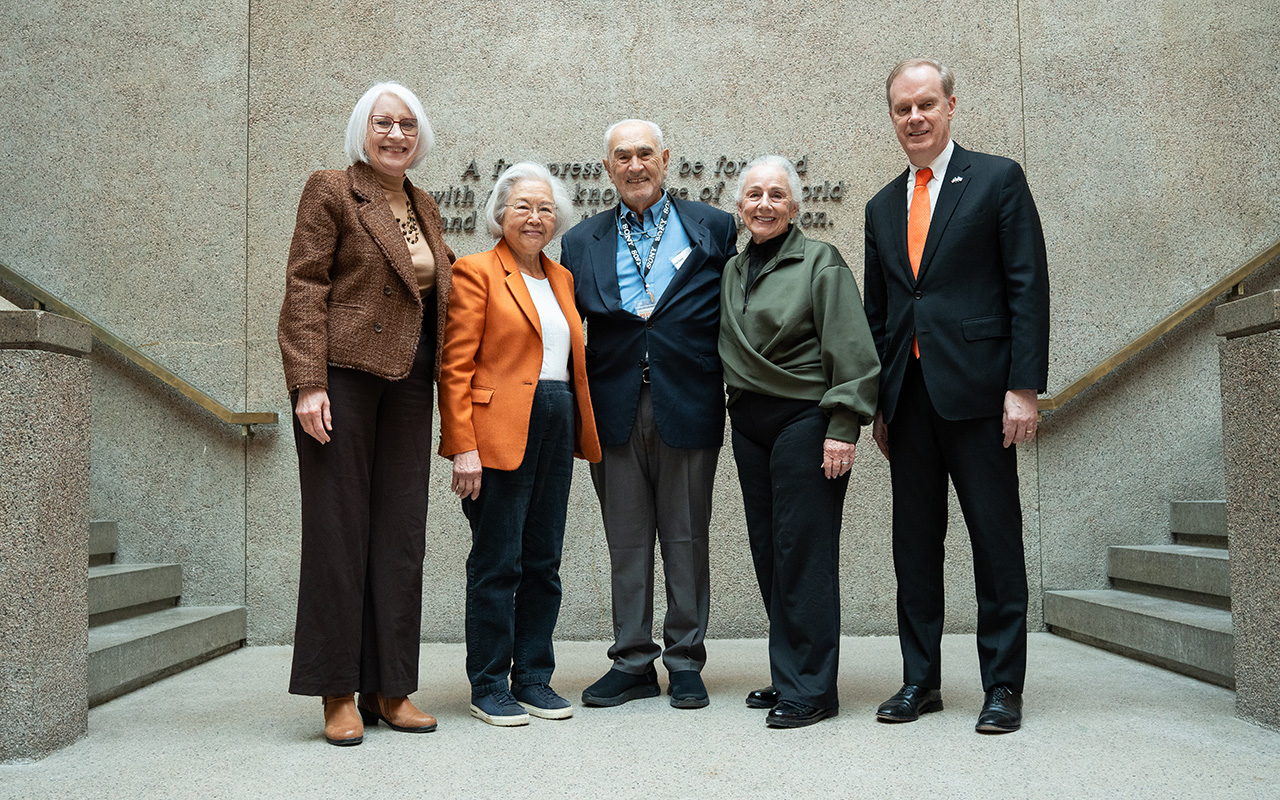 Five people stand together on a stone staircase inside an academic building.