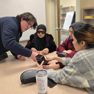 Q-SUCCEED-CNY participants examine a small device during a hands-on workshop session in a classroom setting.