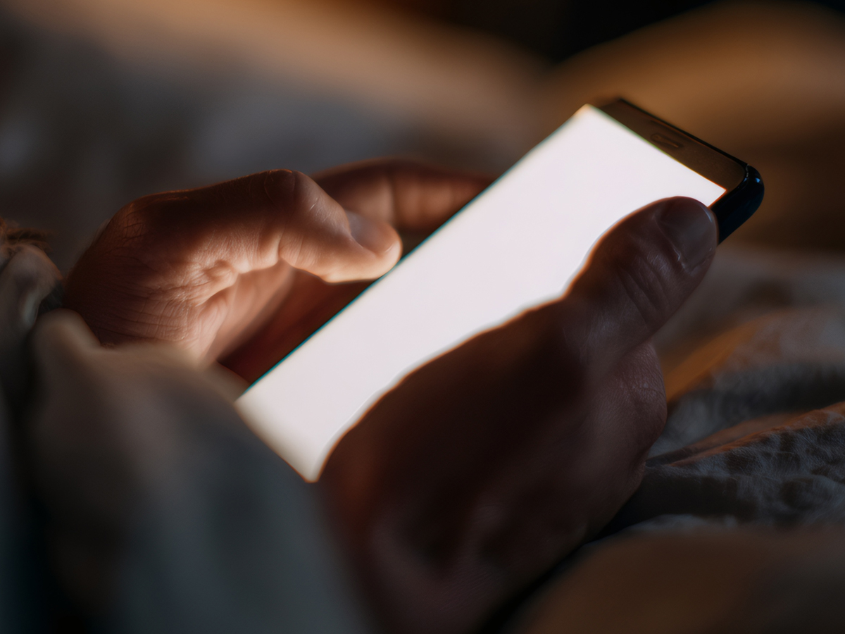 A person checks their phone while laying in bed.