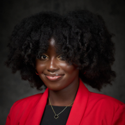 A student smiles wearing a red blazer in a professional headshot photo in front of a grey background