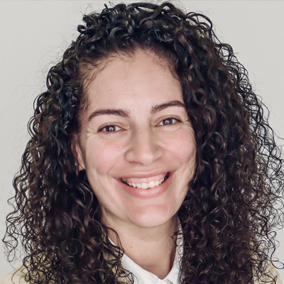 A person smiles in a professional headshot wearing a white collared shirt against a light gray background.