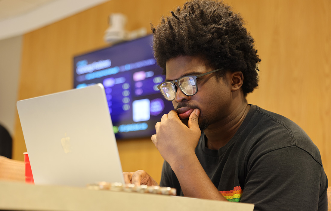 Person seated at a table, concentrating on a laptop during a cybersecurity competition, with a score screen visible in the background.