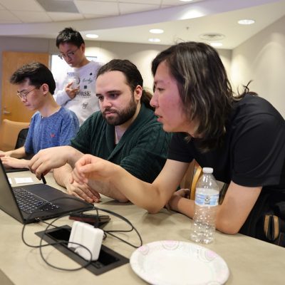 Students collaborating at a table, working together on a laptop during a cybersecurity competition.